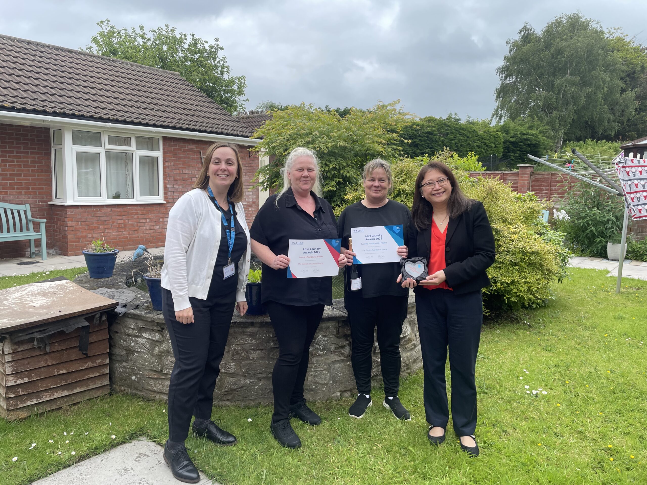 Four women standing in a garden holding a Love Laundry Award and certificate
